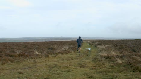 Male-Marathon-Athlete-Running-Away-from-Camera-on-a-Training-Run-Over-Exmoor-UK-4K