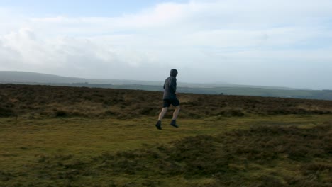Male-Fitness-Athlete-Panning-Shot-of-Runner-Running-and-Training-Over-Moorland-Countryside-Exmoor-UK-4K