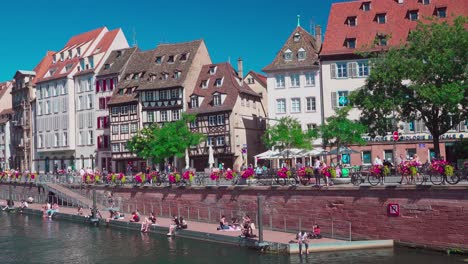 People-sitting-by-the-river-near-Pont-du-Corbeau,-Strasbourg,-Alsace,-France,-on-a-nice,-bright-and-sunny-day