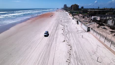 Vista-Aérea-De-Un-Automóvil-Conduciendo-En-La-Playa-De-Daytona,-En-La-Soleada-Florida---Reversa,-Inclinación,-Disparo-De-Drones