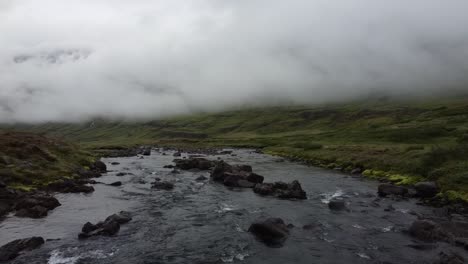 Shallow-rocky-mountain-river-in-Iceland-in-foggy-day,-drone-view-above-water