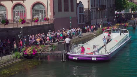 Passengers-disembark-a-half-empty-sightseeing-boat-near-Pont-du-Corbeau,-Strasbourg,-Alsace,-France