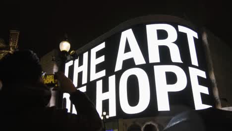 Piccadilly-Circus-In-Der-Nacht-In-London-Mit-Menschen,-Die-Einen-Bildschirm-Mit-Dalai-Lama-Beobachten