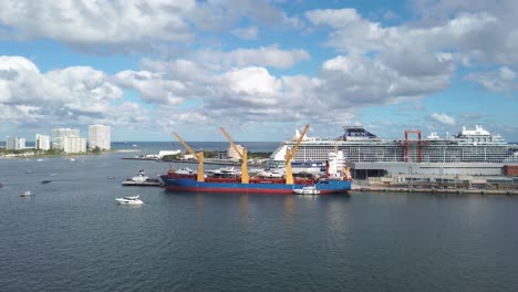 Sunny-Florida-afternoon-in-the-busy-port-with-cargo-ship-unloading,-small-boats-enter-and-exit-the-port-while-a-massive-cruise-ship,-Beyond,-loads-passengers-for-a-cruise