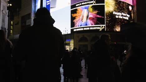 Pan-up-at-people-watching-Piccadilly-Circus-screen-in-central-London-at-night