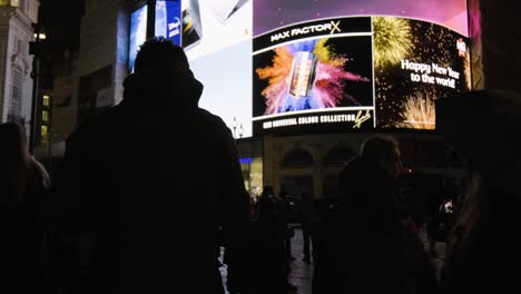 Pan-up-at-people-watching-Piccadilly-Circus-screen-in-central-London-at-night