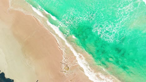 Areal-top-view-video-sequence-of-waves-closing-to-coastline,-crystal-clear-sea-water-splashing-on-sandy-beach,-sunshine-day-and-clear-weather