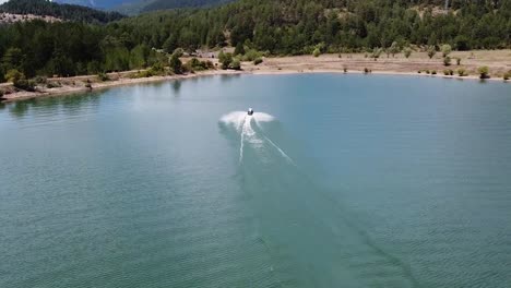 Man-has-fun-on-a-jet-ski-on-a-lake-surrounded-by-pine-forest,-Albania