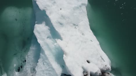 Jokulsarlon-Glacier-Lagoon,-Iceland,-drone-view-of-an-iceberg-melting-in-blue-water