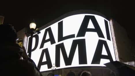 Piccadilly-Circus-at-night-in-London-with-people-watching-screen-showing-Dalai-Lama,-Slow-Motion