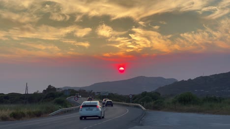 Increíble-Puesta-De-Sol-Con-Un-Sol-Rojo-Y-Nubes-Anaranjadas-En-Una-Carretera-Con-Autos-Que-Pasan-En-España,-Toma-De-4k