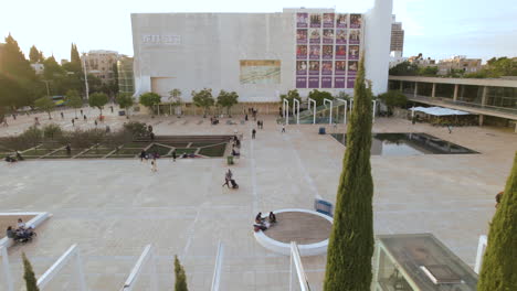 Drone-Deslizándose-Hacia-La-Izquierda-Mientras-La-Gente-Se-Relaja-Y-Descansa-Debajo-Durante-La-Puesta-De-Sol---Plaza-Habima-Tel-Aviv,-Israel