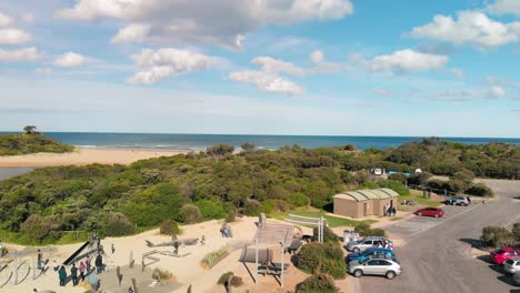 Drone-view-of-a-coastal-town-in-Torquay-showing-trees-and-people-in-park-with-the-background-of-the-ocean