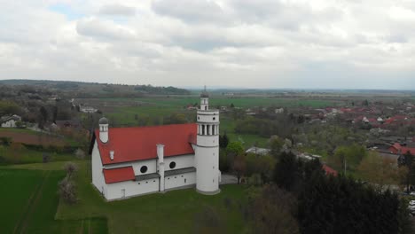 drone-flies-back-at-Church-of-the-Ascension-of-Christ-in-Bogojina,-slovenia-on-cloudy-spring-day