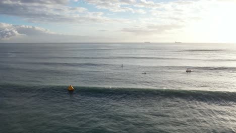 Aerial-view-of-early-morning-swimmers-with-sunshine-lighting-up-Scarborough-Bay,-Sumner