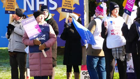 NHS-nurses-strike-for-fair-pay-rights,-waving-banners-and-flags-outside-UK-hospital