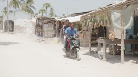 Two-young-black-men-driving-on-motorbike-through-village-in-Africa