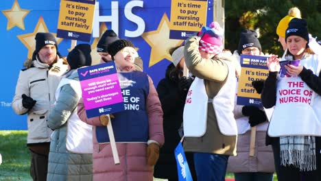 NHS-nurses-strike-for-fair-pay-and-better-care-outside-St-Helens-hospital-on-a-cold-winter-morning,-waving-banners-and-flags