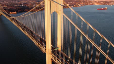 Aerial-overview-tilting-towards-traffic-on-the-sunlit-Verrazzano-Narrows-Bridge,-in-NY,-USA