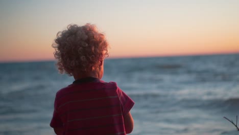 Zeitlupenaufnahme-Eines-Kleinen-Jungen,-Der-Bei-Sonnenuntergang-Steine-Ins-Meer-Wirft