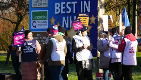 NHS-nurses-strike-for-fair-pay-and-better-healthcare-outside-hospital-on-a-chilly-winter-morning,-waving-banners-and-flags