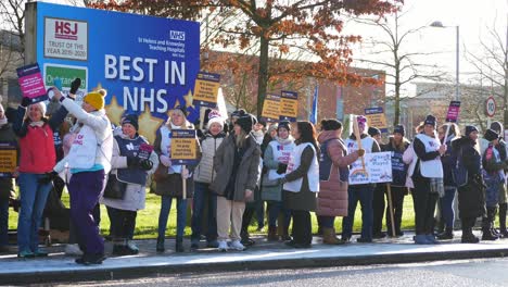 NHS-nurses-strike-for-fair-pay-and-better-care-outside-hospital-on-a-chilly-winter-morning,-waving-banners-and-flags