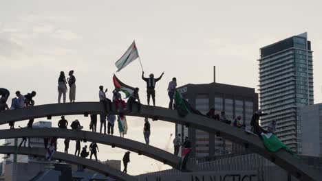 Pro-Palestine-Protesters-waving-flag-on-arch-in-Nathan-Phillips-Square,-Toronto