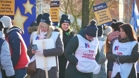 Overworked-NHS-nurses-strike-for-fair-pay-and-better-care-outside-St-Helens-hospital-on-a-chilly-winter-morning,-waving-banners-and-flags