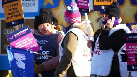 NHS-nurses-strike-for-fair-pay,-waving-banners-and-flags-outside-UK-hospital,-Merseyside