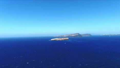 Vista-Aérea-4k-Azul-Del-Mar-Y-El-Cielo-Hacia-Islas-Tropicales-Distantes-En-Movimiento-Horizontal-En-Santorini-Grecia