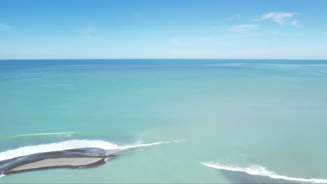 High-aerial-of-beautiful-turquoise-colored-Rakaia-River-meeting-ocean-and-lone-surfer