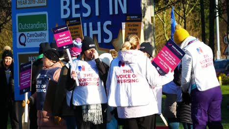 NHS-nurses-strike-for-fair-pay-and-better-care-service-outside-St-Helens-hospital-on-a-chilly-winter-morning,-waving-banners-and-flags