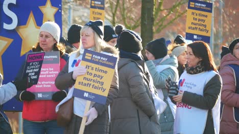 NHS-nurses-strike-for-fair-pay-outside-St-Helens-hospital-on-a-chilly-winter-morning,-waving-banners-and-flags