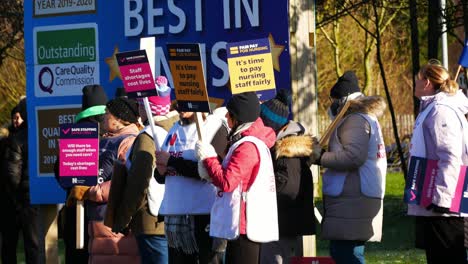 NHS-nurses-strike-for-fair-pay-and-better-care-service-outside-hospital-on-a-chilly-winter-morning,-waving-banners-and-flags