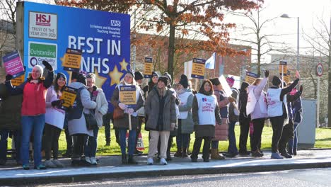 NHS-nurses-strike-for-fair-pay-and-better-care-outside-St-Helens-hospital-on-a-winter-morning,-waving-banners-and-flags