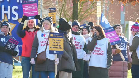 UK-NHS-nurses-strike-for-fair-pay-and-better-care-outside-St-Helens-hospital-on-a-chilly-winter-morning,-waving-banners-and-flags