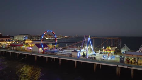 Aerial-view-close-to-the-Illuminated-rides-at-the-Galveston-Island-Historic-Pleasure-Pier,-dusk-in-Texas,-USA