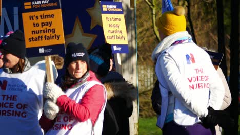 NHS-nurses-strike-picket-line-for-fair-pay-and-better-care-outside-St-Helens-hospital-on-a-chilly-winter-morning,-waving-banners-and-flags