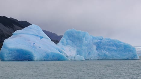 Glaciar-Azul-Flotando-Con-Una-Montaña-A-Sus-Espaldas-Y-Niebla-Como-Fondo