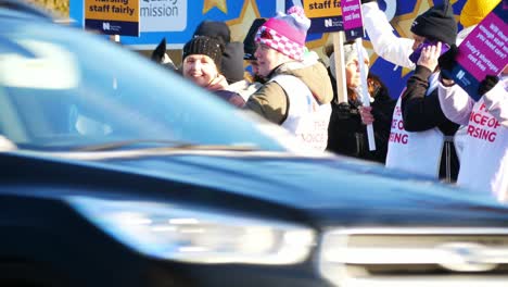 NHS-nurses-strike-for-fair-pay,-waving-banners-and-flags-outside-UK-hospital,-St-Helens