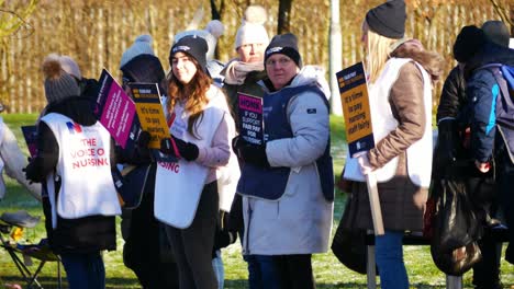 NHS-nurses-strike-in-solidarity-for-fair-pay-and-better-care-outside-St-Helens-hospital-on-a-chilly-winter-morning,-waving-banners-and-flags