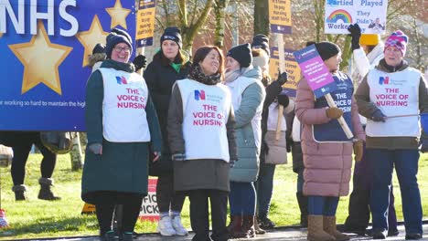 NHS-nurses-strike-for-fair-pay,-waving,-holding-banners-and-flags-outside-UK-hospital