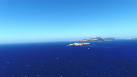 Vista-Aérea-4k-Azul-Del-Mar-Y-El-Cielo-Hacia-Islas-Tropicales-Distantes-En-Santorini-Grecia