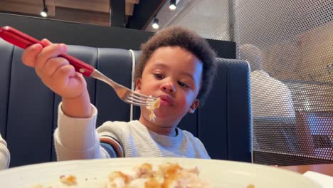 Two-year-old-black-baby,-mix-raced,-learns-how-to-use-the-fork-correctly-in-a-restaurant-seated-next-to-his-mother
