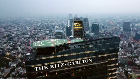 Incline-Hacia-Abajo-La-Vista-Aérea-De-La-Torre-De-Cristal-Del-Hotel-Ritz-carlton-En-La-Ciudad-De-México-En-Una-Puesta-De-Sol-épica,-Arquitectura-Contrastante,-Helipuerto-Verde