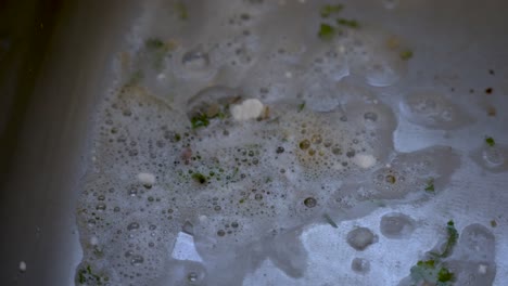 Close-Up-Of-Dirty-Water-With-Food-Bits-Draining-Down-Kitchen-Sink-Hole