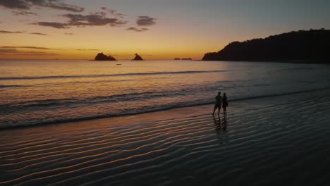 Paar,-Das-Während-Des-Sonnenuntergangs-Am-Ufer-Des-Meeres-In-Guanacaste-Beach,-Costa-Rica-Steht---Drohnenaufnahme