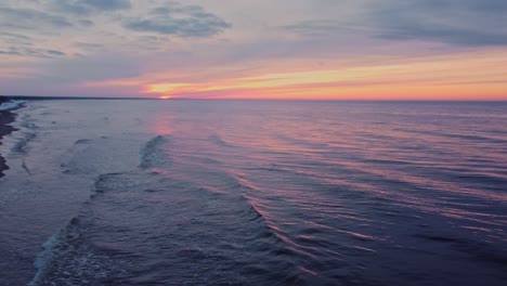 Aerial-drone-flying-low-above-baltic-sea-water-at-sunset,-airplane-on-sky