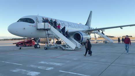 Slow-panning-shot-of-a-passengers-disembarking-from-a-plane-onto-the-tarmac-on-a-clear-cloudless-day