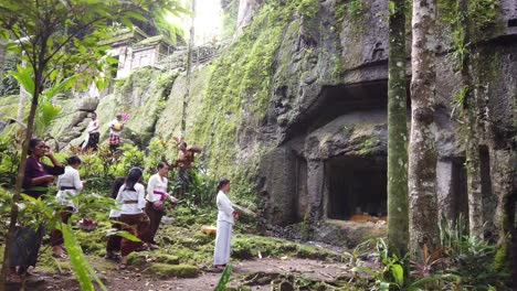 Gente-Balinesa-Rezando-En-El-Templo-De-Goa-Garba,-Antigua-Cueva-Arqueológica-De-Piedra,-Vistiendo-Ropas-Tradicionales,-Sarong-De-La-Cultura-Hindú-De-Bali,-Tampaksiring,-Gianyar